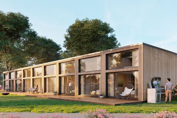 Moderne Holzhaus mit großen Fenstern, umgeben von Bäumen und bunten Blumen.